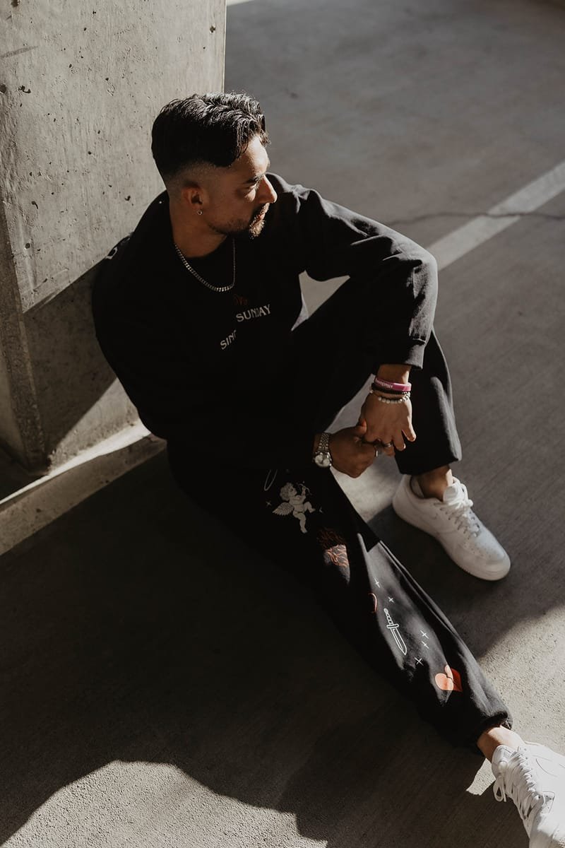 A model seated against a concrete wall in the Sinner Sunday crewneck and cherub sweatpants