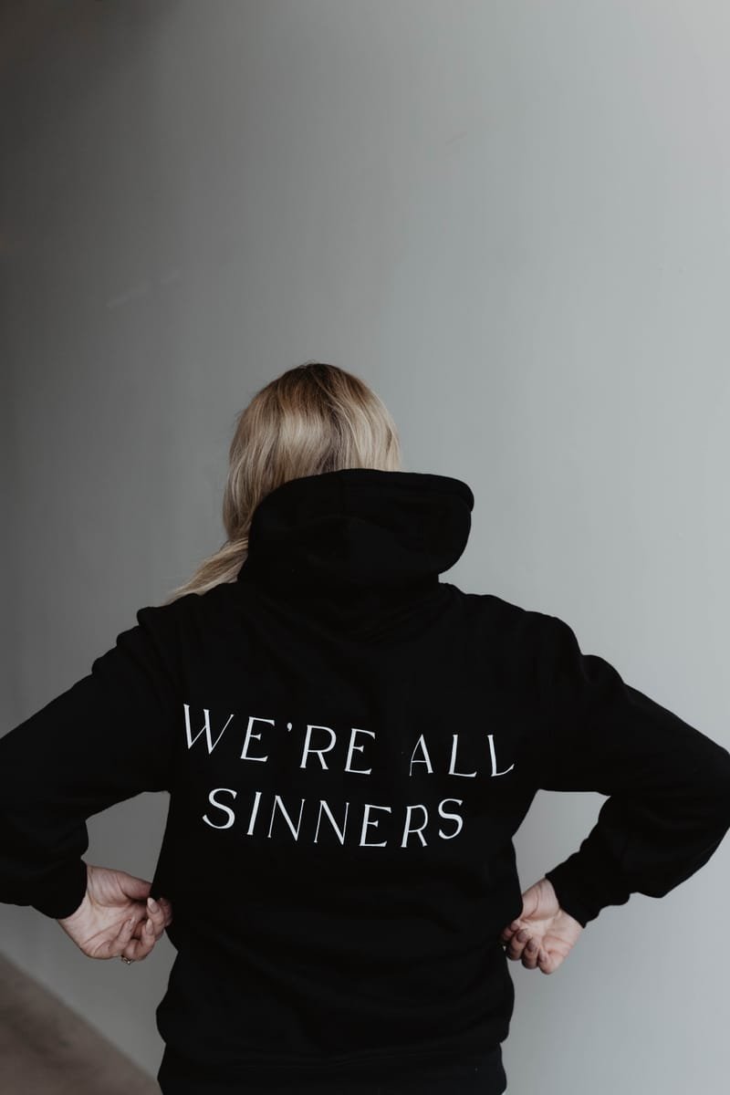 The back of the black Sinner Sunday hoodie reading WE'RE ALL SINNERS